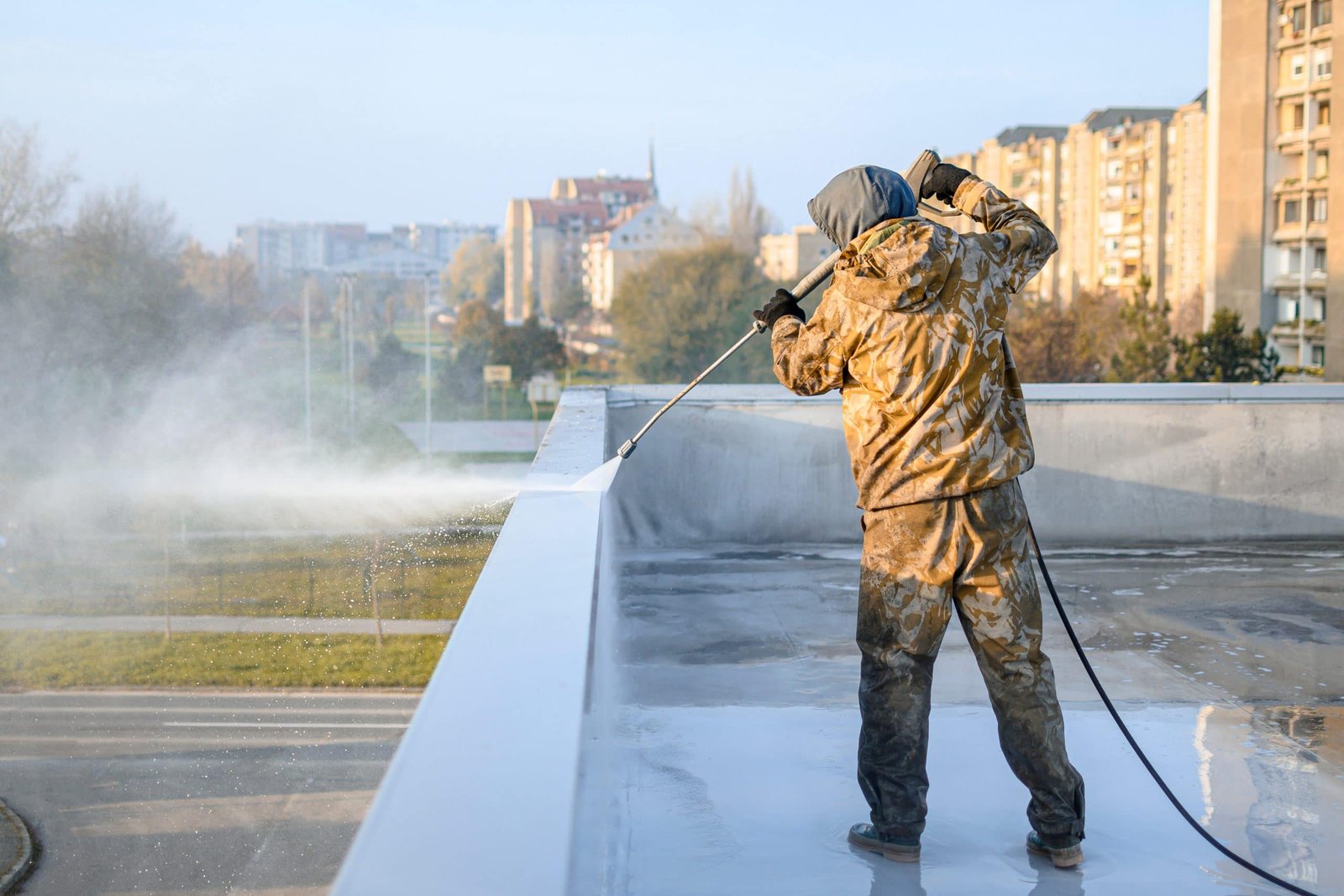 A man in camouflage is spraying water on a roof.