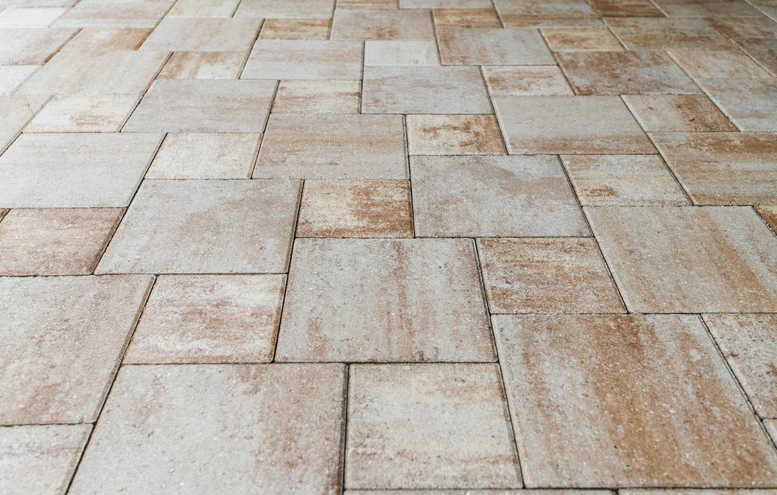 The image shows a floor made of light brown and beige stone tiles arranged in a staggered pattern. The tiles have a textured surface and natural color variations, creating a rustic look.