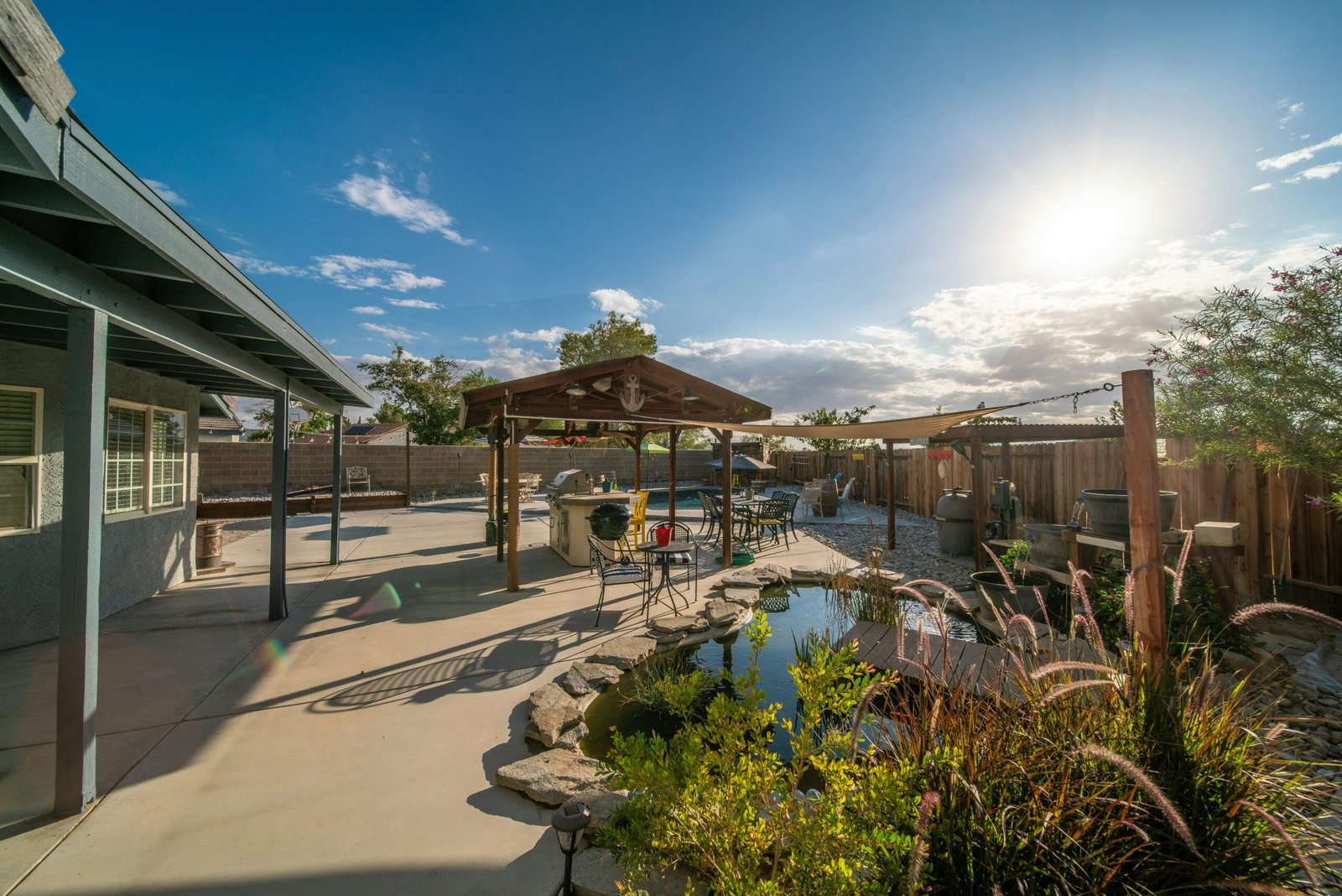 Residential backyard paver patio with a small pond and gazebo, desert-style landscaping