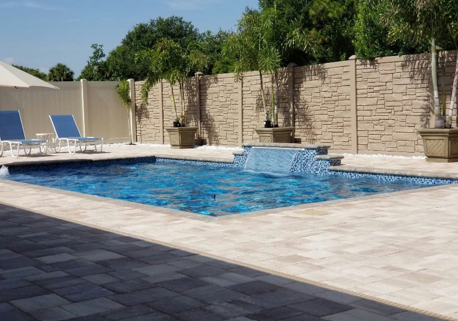 Luxury backyard pool surrounded by two-tone gray and tan paver decking
