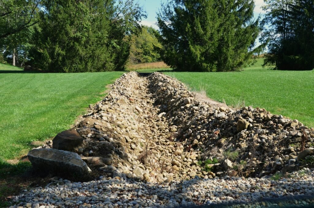 Stone-filled drainage swale carrying water across a residential lawn