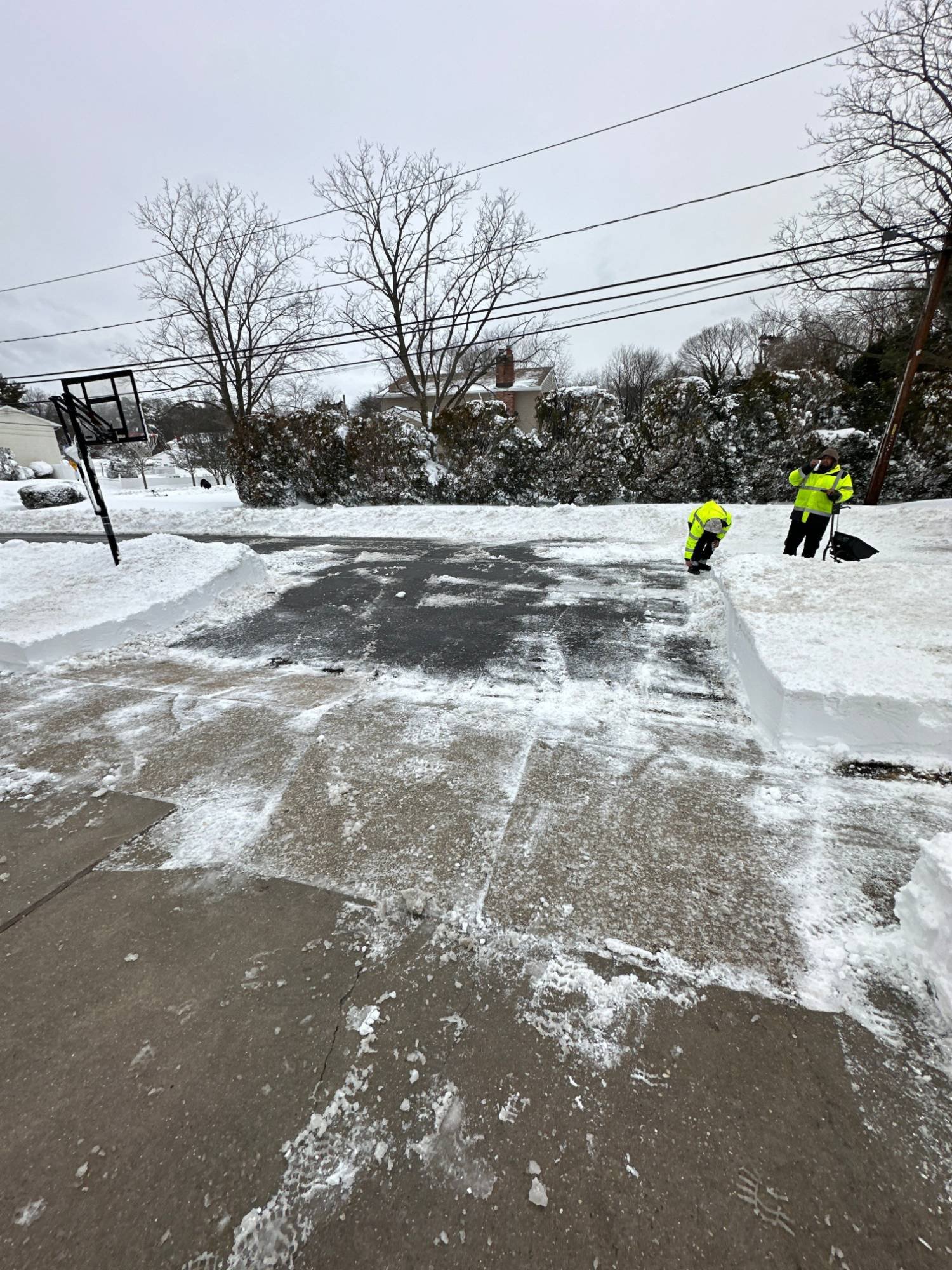Two crew members in high-visibility jackets clearing snow at the end of a driveway